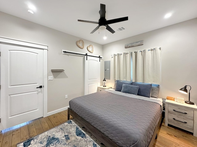 bedroom featuring light wood-type flooring, visible vents, a ceiling fan, a barn door, and baseboards