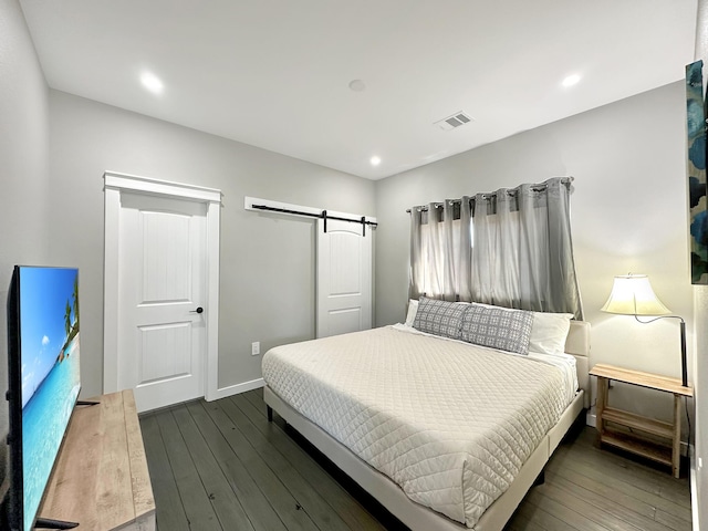 bedroom featuring a barn door, baseboards, visible vents, and dark wood-style flooring