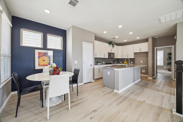 kitchen with stainless steel microwave, backsplash, visible vents, and a kitchen island with sink