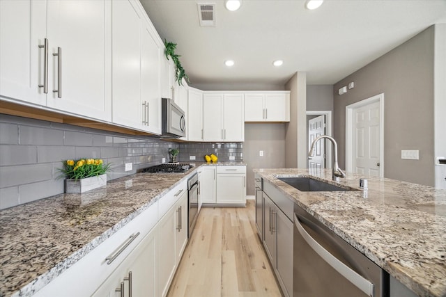 kitchen with a sink, stainless steel appliances, light stone counters, and white cabinets