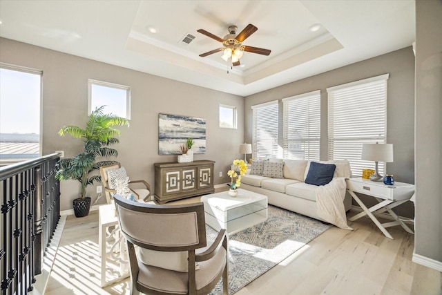 living room featuring a tray ceiling, a healthy amount of sunlight, and light wood-style flooring