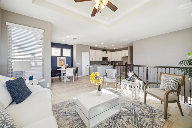 living room with recessed lighting, light wood-style flooring, baseboards, and a tray ceiling