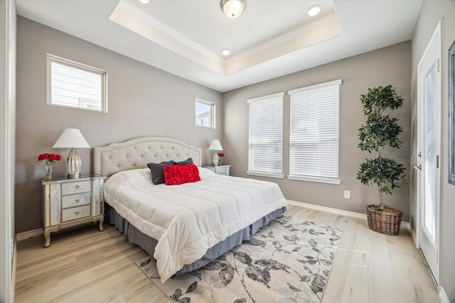 bedroom with crown molding, baseboards, light wood-type flooring, and a tray ceiling