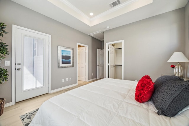 bedroom featuring wood finished floors, baseboards, visible vents, a tray ceiling, and ornamental molding