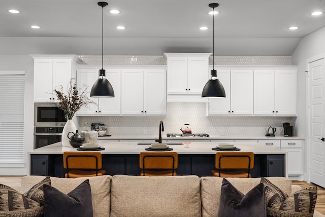 kitchen with stainless steel appliances, decorative backsplash, light countertops, white cabinetry, and a kitchen breakfast bar