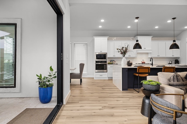 kitchen featuring stainless steel appliances, light countertops, white cabinets, tasteful backsplash, and light wood-type flooring