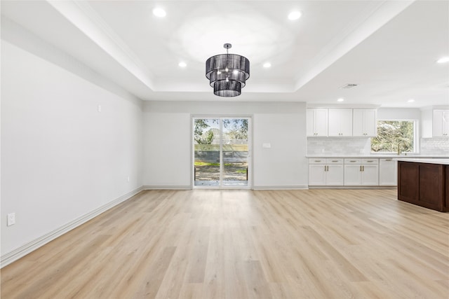 unfurnished living room featuring baseboards, recessed lighting, ornamental molding, a raised ceiling, and light wood-type flooring