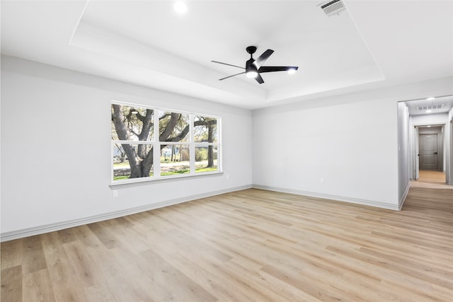 unfurnished room featuring light wood-type flooring, a raised ceiling, visible vents, and a ceiling fan