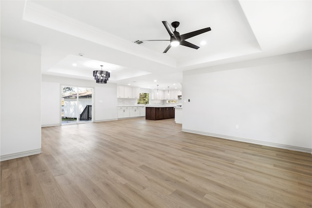 unfurnished living room with ceiling fan with notable chandelier, baseboards, light wood-type flooring, and a tray ceiling