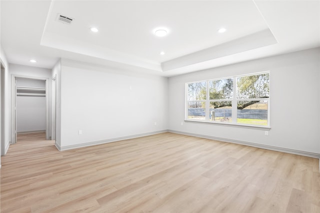 spare room featuring visible vents, light wood-style floors, and a tray ceiling