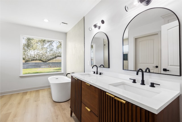 full bathroom featuring a soaking tub, wood finished floors, double vanity, and a sink