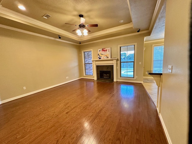 unfurnished living room with visible vents, a fireplace with flush hearth, a tray ceiling, wood finished floors, and a textured ceiling