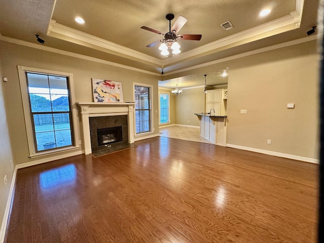 unfurnished living room with a fireplace with flush hearth, a raised ceiling, ceiling fan with notable chandelier, wood finished floors, and baseboards