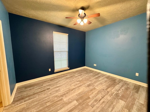 spare room featuring a textured ceiling, wood finished floors, baseboards, and ceiling fan