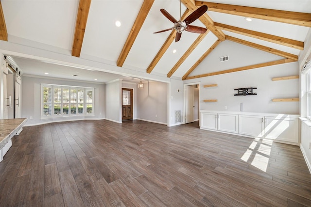 unfurnished living room featuring visible vents, ceiling fan, beamed ceiling, a barn door, and dark wood-style flooring