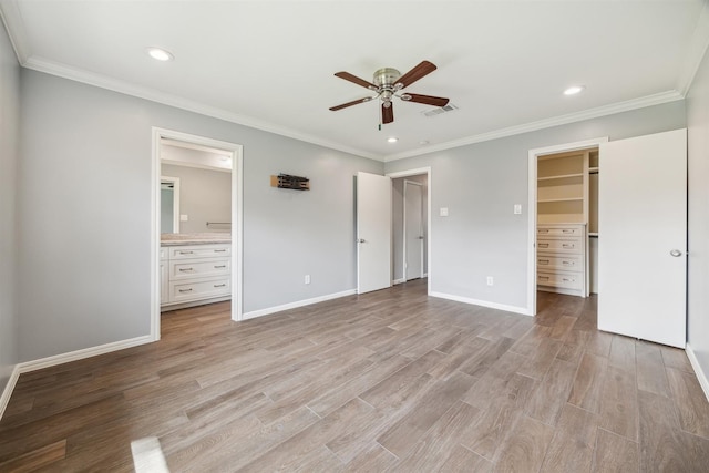 unfurnished bedroom featuring visible vents, a walk in closet, crown molding, light wood finished floors, and baseboards