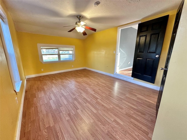 spare room featuring light wood finished floors, a textured ceiling, baseboards, and a ceiling fan