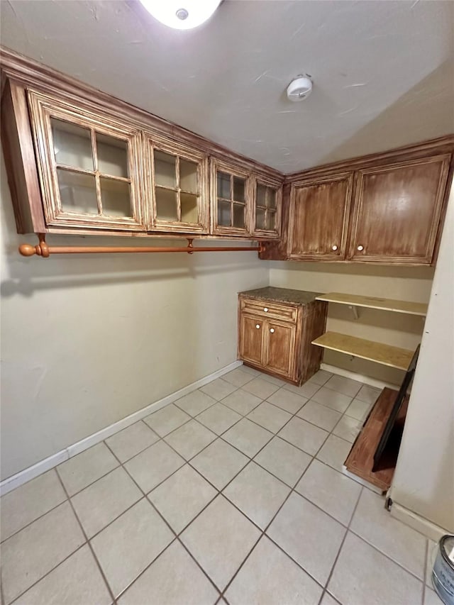 interior space featuring light tile patterned floors, glass insert cabinets, brown cabinets, and baseboards