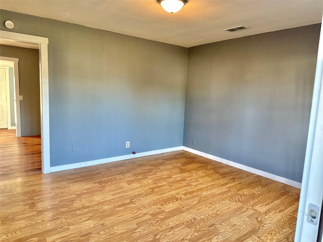 empty room featuring visible vents, baseboards, a textured ceiling, and wood finished floors