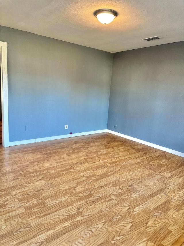 unfurnished room featuring visible vents, a textured ceiling, baseboards, and wood finished floors