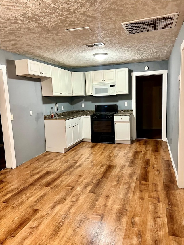 kitchen with black gas range oven, visible vents, white microwave, white cabinets, and light wood-type flooring