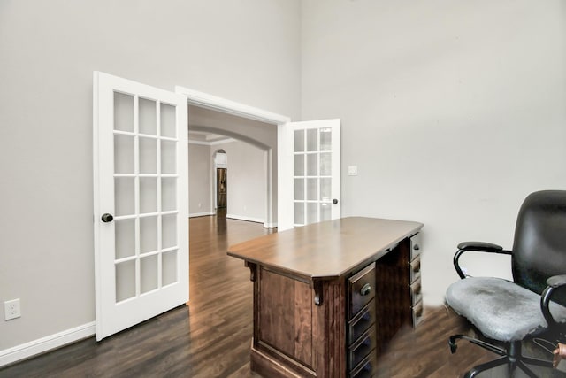 home office featuring baseboards, arched walkways, dark wood-type flooring, french doors, and a towering ceiling