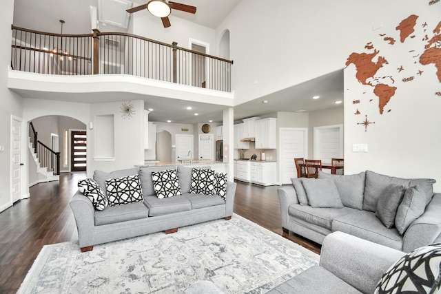 living area with dark wood finished floors, stairs, arched walkways, and ceiling fan