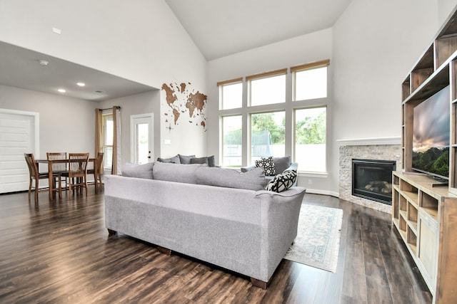 living area featuring baseboards, high vaulted ceiling, a stone fireplace, and dark wood-style floors