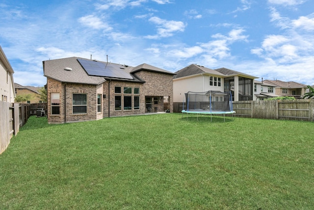 back of house featuring a trampoline, a fenced backyard, a yard, brick siding, and solar panels