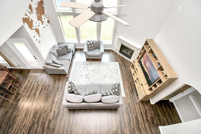 living area featuring wood finished floors, a glass covered fireplace, a towering ceiling, baseboards, and ceiling fan