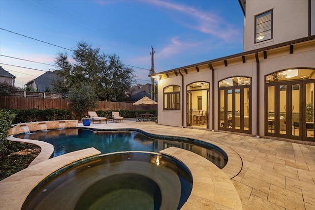 pool at dusk with a patio area, french doors, fence, and a pool with connected hot tub