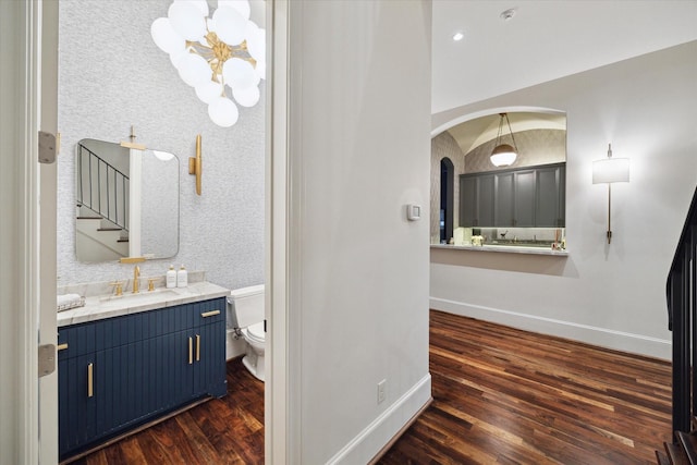 bathroom with a notable chandelier, toilet, wood finished floors, and baseboards