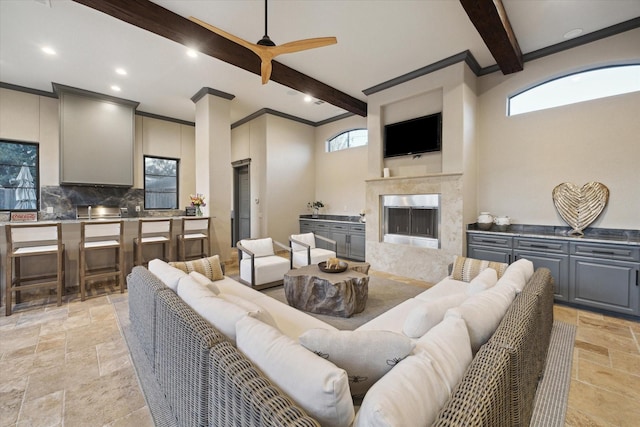 living area featuring stone tile flooring, beamed ceiling, ceiling fan, and a premium fireplace