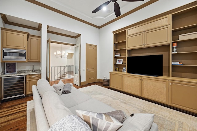 living room featuring dark wood-type flooring, beverage cooler, ornamental molding, ceiling fan with notable chandelier, and indoor bar