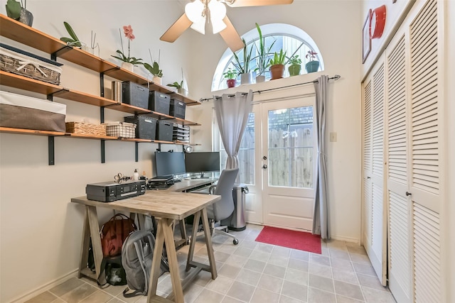 office featuring light tile patterned floors, baseboards, a ceiling fan, and a towering ceiling