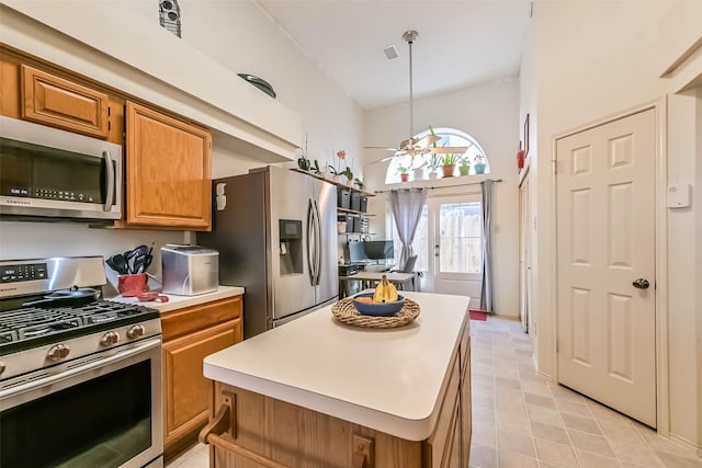 kitchen with a ceiling fan, a kitchen island, light countertops, appliances with stainless steel finishes, and brown cabinets