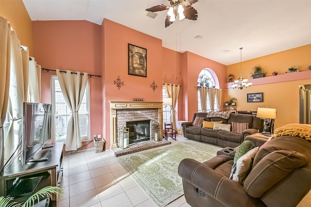 tiled living area with a brick fireplace, ceiling fan with notable chandelier, visible vents, and high vaulted ceiling