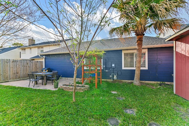 rear view of house featuring a patio, fence, a lawn, and roof with shingles