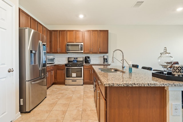 kitchen featuring visible vents, a sink, backsplash, appliances with stainless steel finishes, and brown cabinetry