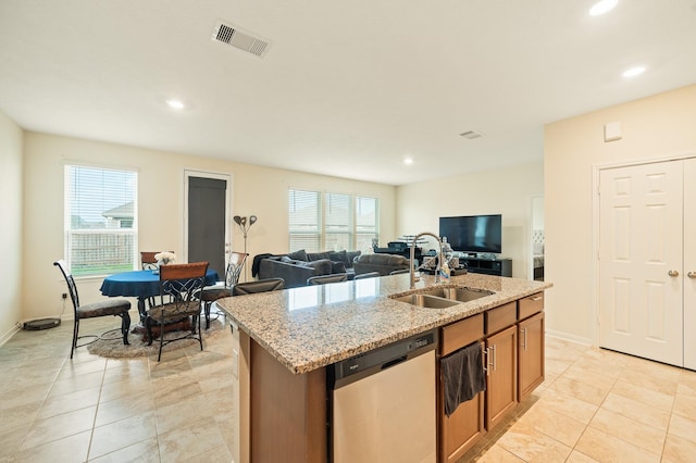 kitchen with light stone countertops, a center island with sink, visible vents, a sink, and stainless steel dishwasher