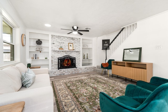 living room with built in shelves, wood finished floors, stairs, a textured ceiling, and a brick fireplace