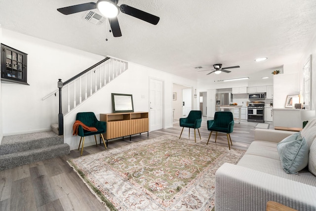 living room with visible vents, a textured ceiling, light wood-style floors, baseboards, and stairs