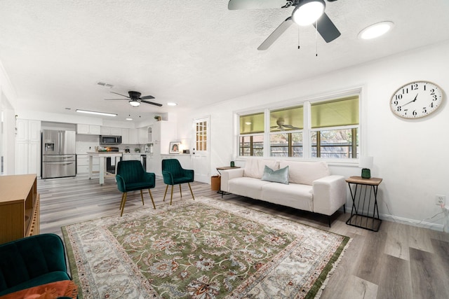 living room featuring light wood-type flooring, visible vents, baseboards, and a textured ceiling