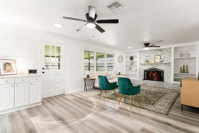 living room with light wood-type flooring, built in shelves, visible vents, a textured ceiling, and a brick fireplace