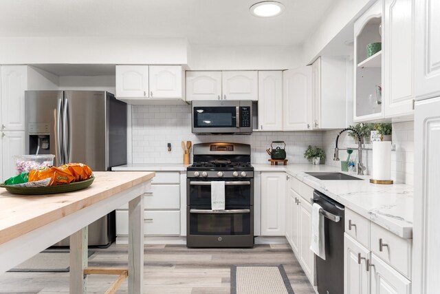 kitchen with light stone countertops, light wood-style flooring, a sink, stainless steel appliances, and white cabinets