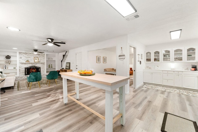 kitchen with light wood-type flooring, visible vents, white cabinetry, a fireplace, and glass insert cabinets