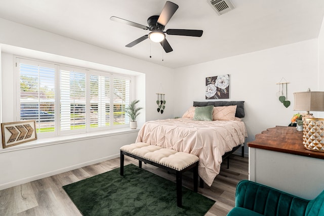 bedroom with ceiling fan, visible vents, baseboards, and wood finished floors