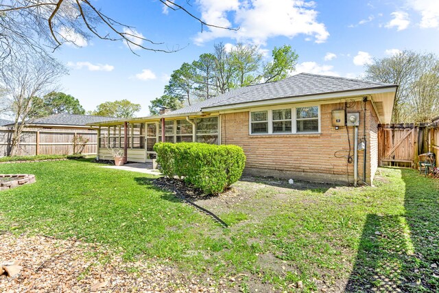 back of property with a yard, brick siding, roof with shingles, and a fenced backyard