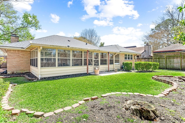 rear view of property featuring brick siding, fence, a chimney, a yard, and a sunroom