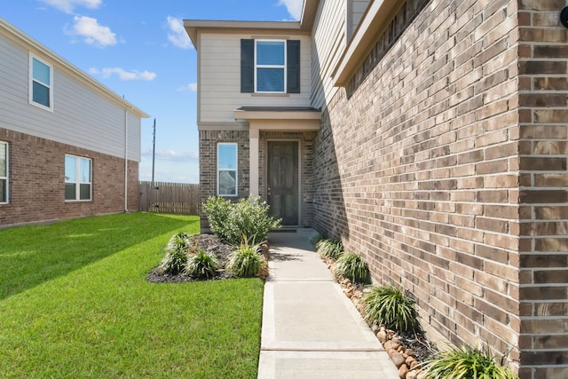 entrance to property featuring a yard, fence, and brick siding